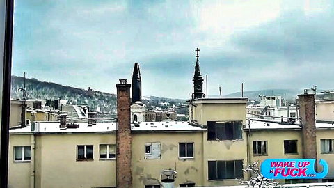 Snowy urban cityscape with church spire viewed from window under cloudy sky with wake up fuck text overlay