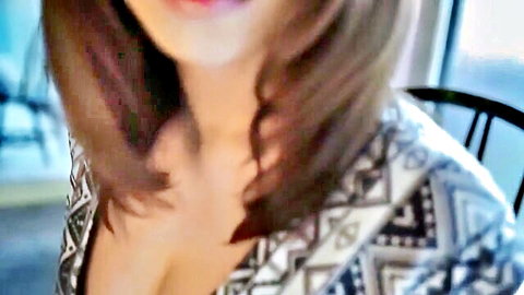 Sexy Japanese brunette babe with long hair smiling and teasing deep cleavage in patterned low-cut top