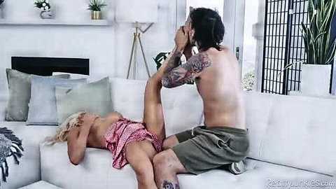 Blonde MILF in pink dress dominated by tattooed stud on couch