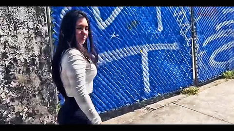 Curvy Latina walking in tight leggings and off-shoulder top by graffiti wall