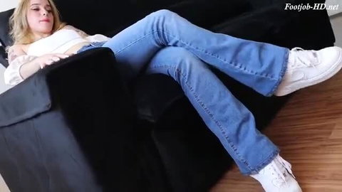 Blonde tattooed girl lounging in jeans and white sneakers, feet fetish tease