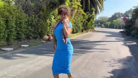 Curvy brunette stepmom in tight blue dress dances with dog outdoors