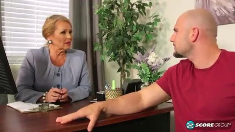 Blonde mature MILF in office suit with bald hunk in red tee gesturing