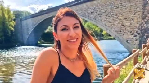 Stella Love smiling by river bridge in black dress