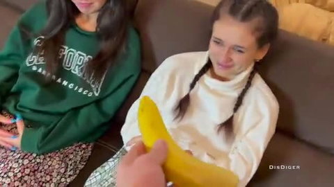 Two sexy teen beauties with pigtails holding banana on couch