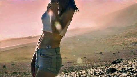 Lena Anderson posing in white crop top and denim shorts on sunny beach