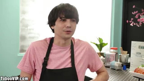 Liza Shay in pink shirt and apron at counter, smiling seductively