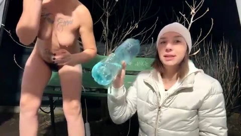 Nude tattooed trans woman holds huge blue dildo with clothed girl in snowy park