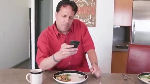 Mature man in red shirt checks phone at dinner table, ignoring mom