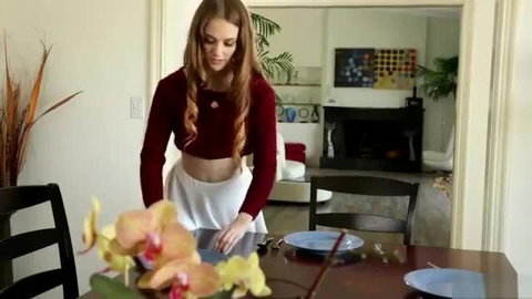 Blonde teen in red crop top and mini skirt arranges flowers at table