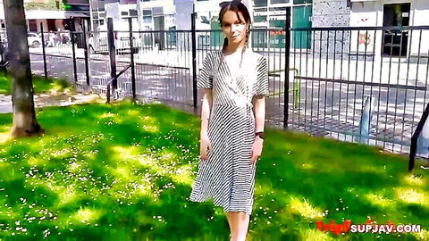 Slim Asian woman in striped wrap dress posing outdoors in park