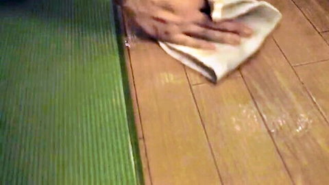 Hands wiping white stains from wooden floor with towel next to green mat