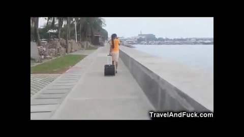 Sexy Filipina flight attendant in orange top and skirt walking with luggage by beach