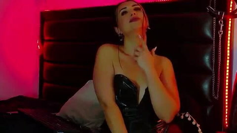 Raveen Noir in sexy black latex dress on bed, seductive pose