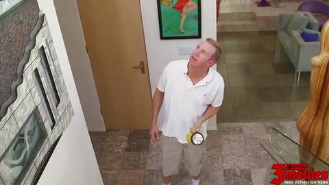 Balding man in white polo and shorts holding banana by door in luxury home