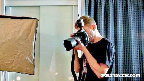 Photographer holding professional camera in Private.com studio with softbox light and blue curtains