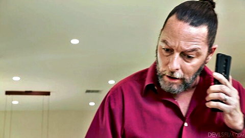 Surprised bearded man with man bun talking on phone in maroon shirt