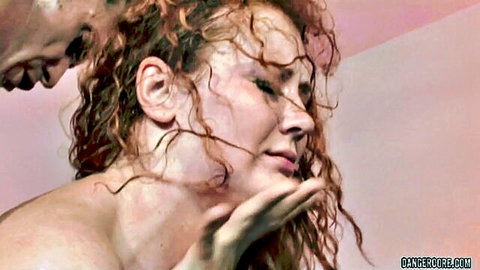Redhead MILF with curly hair gripped by hand, mouth open moaning nude shoulders closeup