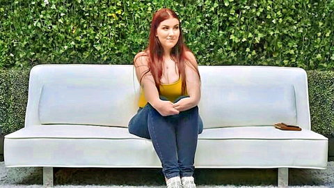 Curvy redhead in yellow tank top and jeans smiling on couch