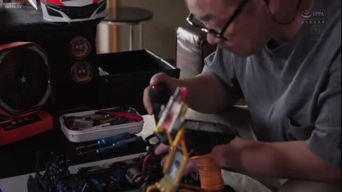 Asian man in glasses assembles RC car toy, worktable setup