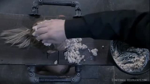 Blonde woman locked in metal case gets face smeared with white goo in BDSM scene