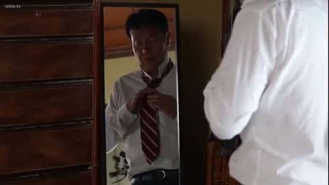 Handsome Asian man in suit tying red striped tie in mirror
