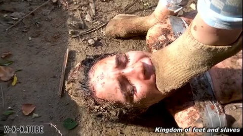 Muddy woman face crushed under dirty socked feet in outdoor foot domination