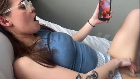 Trinity Olsen in glasses holds phone, open mouth on bed, hot teen tease