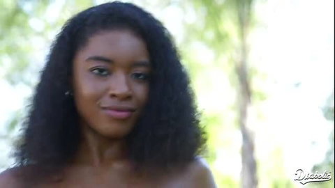 Beautiful black woman with curly hair smiling topless outdoors