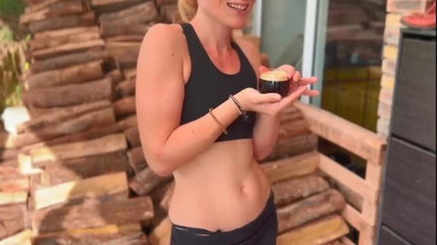 Fit blonde MILF in sports bra and leggings holds jar by wood stack