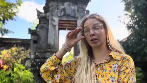 Blonde in floral yellow shirt shades eyes at Bali temple gate