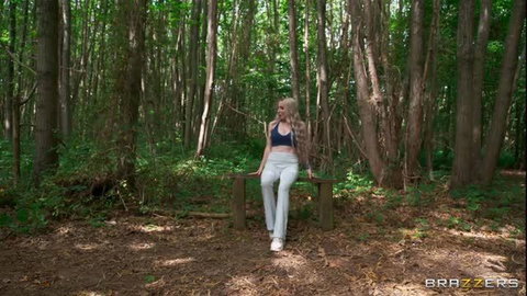 Blonde bombshell in sports bra and leggings sits on bench in forest
