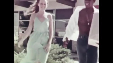 Blonde in green dress walks with smiling black man outdoors
