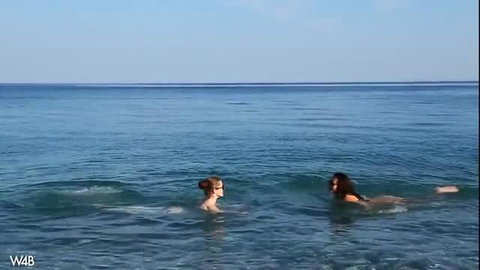 Two nude friends swimming naked in clear sea, sunny beach vibes