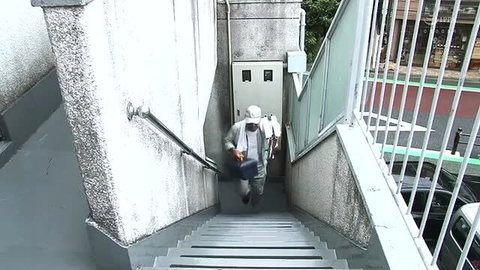 Asian man in hazmat suit descends stairs in urban outdoor scene
