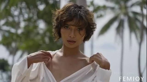 Tanned beauty with wavy brunette hair strips sheer blouse on beach