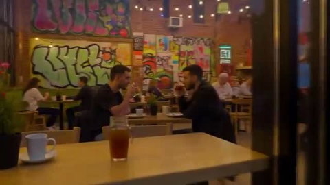 Two fit college guys in casual clothes chat intensely at urban cafe table