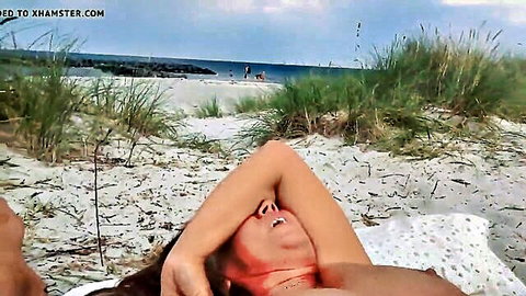 Brunette woman nude on beach, arms raised in ecstasy during solo masturbation