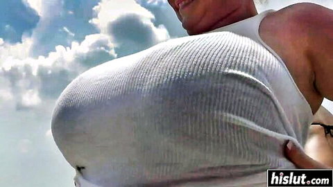 Busty woman pulling down white tank top to reveal massive tits outdoors