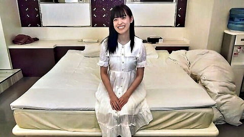 Cute Japanese amateur in button-up white dress sitting smiling on bed
