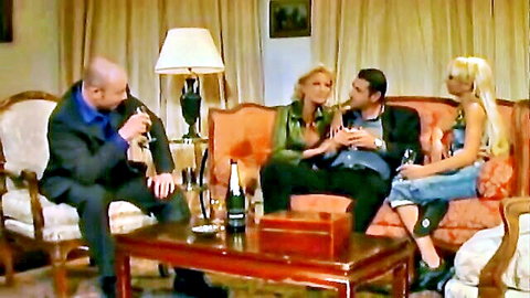 Two suited men chatting with two sexy blondes holding champagne glasses in luxurious living room