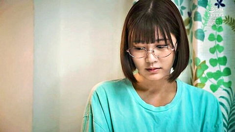 Cute young Japanese brunette with bangs and glasses looking down in oversized blue tee