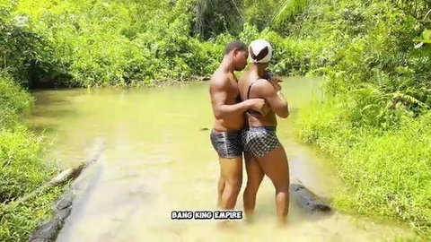 Muscular black BBC couple embracing in swimsuits by jungle stream