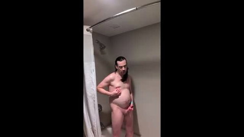 Naked man with long dark hair holding penis in shower