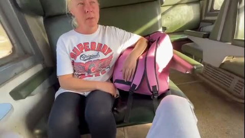 Blonde mature woman in white t-shirt on train with pink backpack