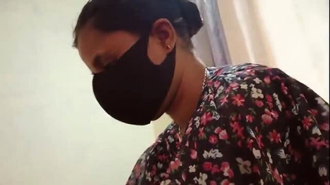 Woman in black face mask wearing floral top, looking down