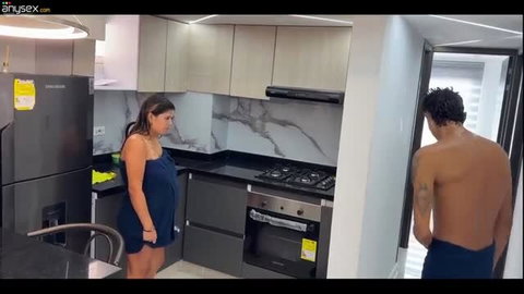 Pregnant woman in blue dress stands in kitchen with shirtless man