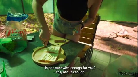 Brunette in black top and denim shorts slicing bread at campsite