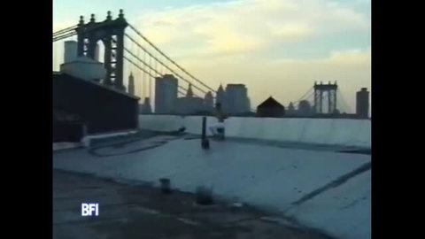 Outdoor rooftop humiliation scene with Manhattan bridge skyline
