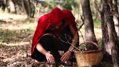 Woman in red hood squatting in woods collecting items